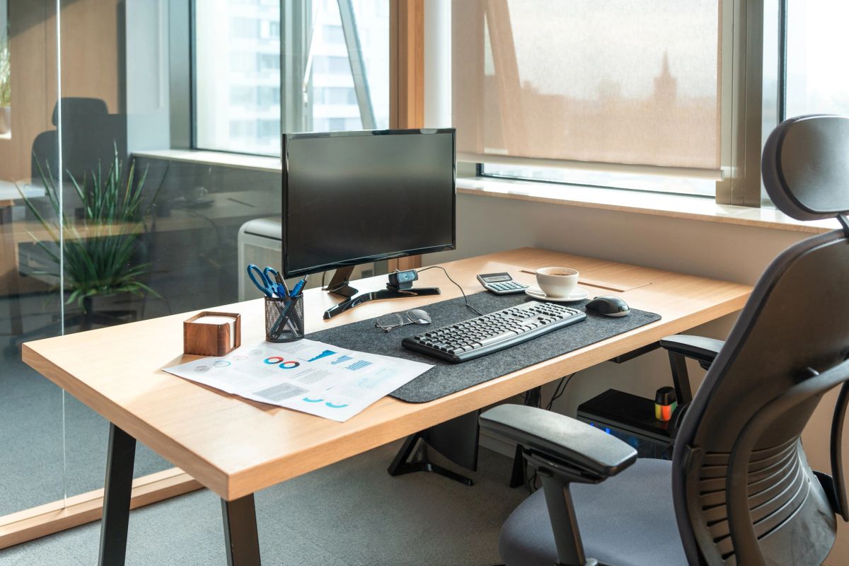 A tidy desk with a monitor, keyboard, calculator and a printed financial report